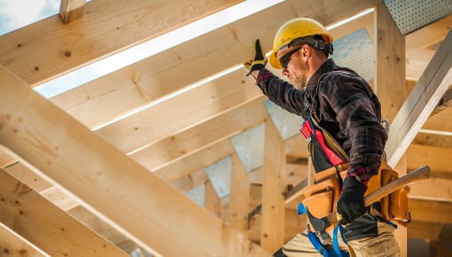 Homme avec des outils de contruction en train de travailler sur la charpente de bois d'un toit de maison.