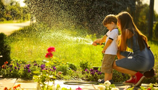 Une mère et son fils arrosent les fleurs du jardin à l'aide d'un arrosoir manuel.